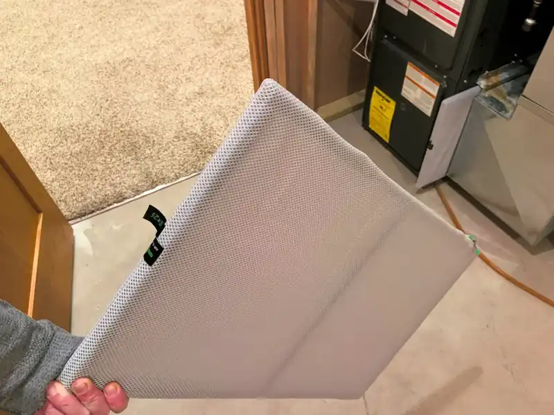 Pleated HVAC air filter being removed next to a furnace