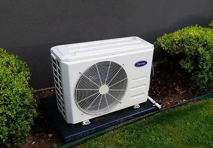 Outdoor split heat pump unit on a pad beside shrubs